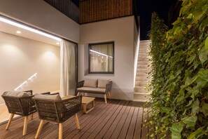 A modern outdoor seating area with wicker furniture and a wooden table, adjacent to a staircase and a wall with a window. - Liiiving in Porto - Pool Paradise Apartment C (Porto)