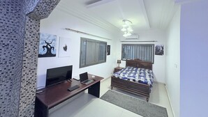 A bedroom with a bed, a desk with a computer, a TV, and artwork on the walls. - Haysym (Dakar)