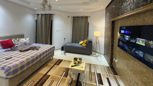 A modern hotel room with a bed, a sofa, a TV mounted on the wall, and a ceiling fan. - Haysym (Dakar)