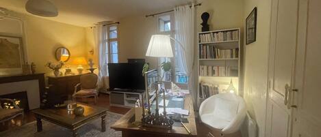 Una sala de estar con televisión, estantería, una silla blanca y una mesa de centro.