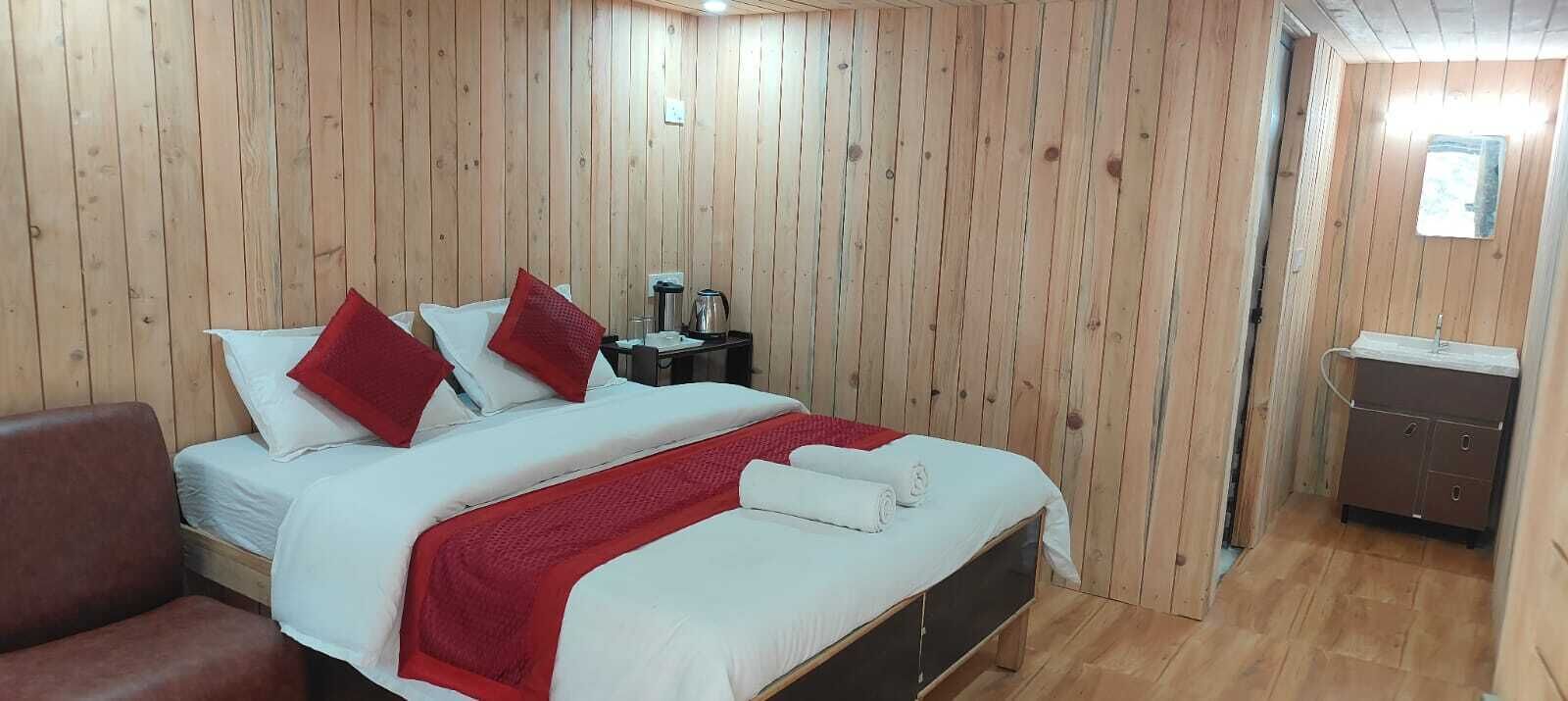A wooden-paneled room with a bed, a nightstand, a chair, and a small bathroom area.