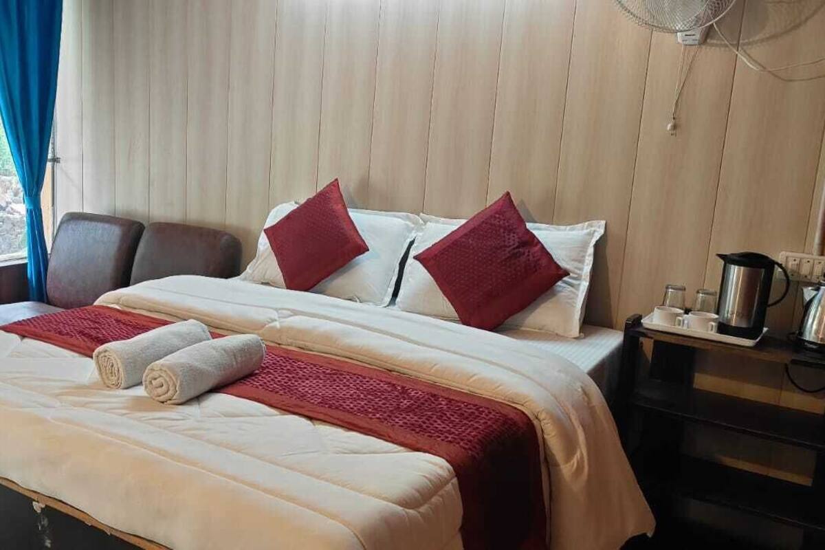 Quarto de hotel com uma cama, uma cadeira, mesa de cabeceira com chaleira e janela com cortinas.