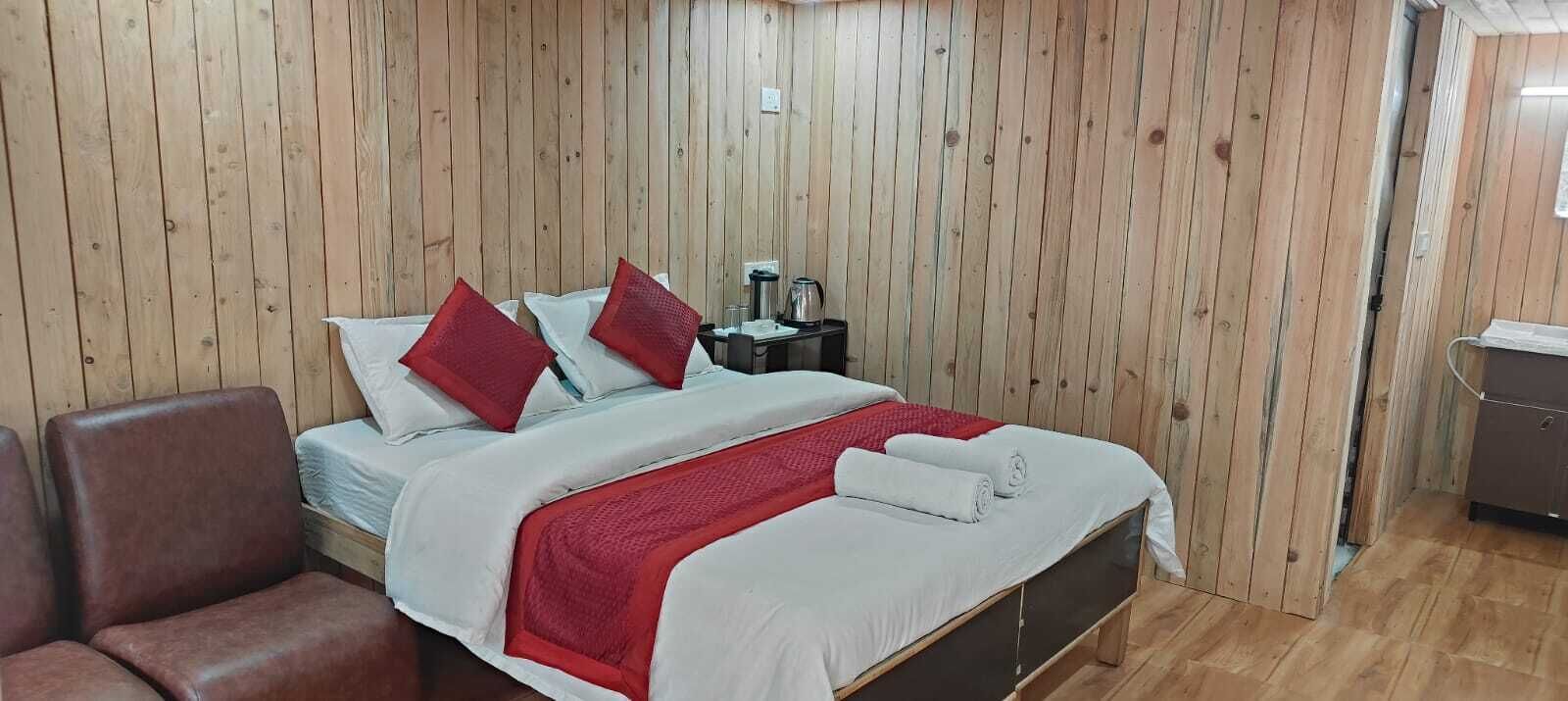 Una habitación con paneles de madera, una cama, una silla, una mesita de noche y una pequeña mesa.