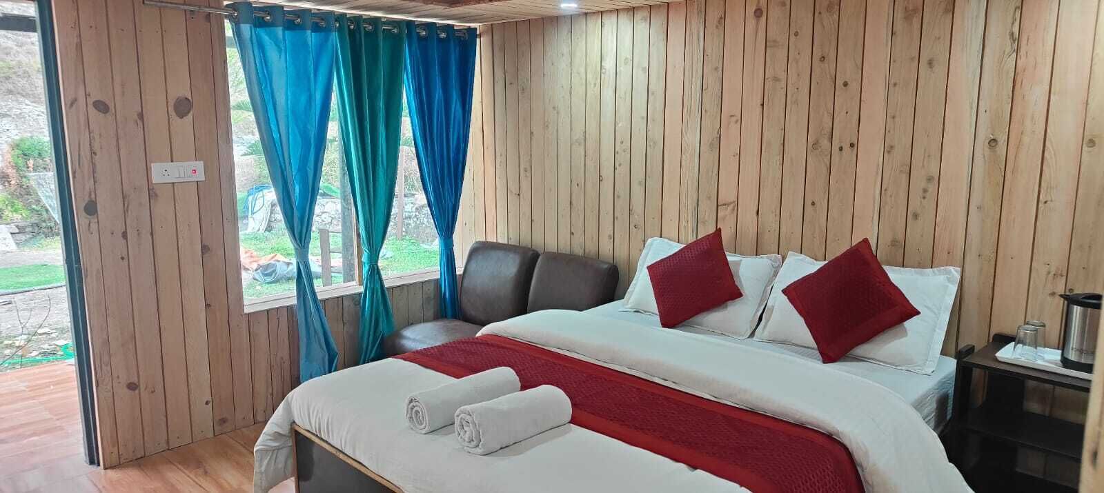 Una habitación con paneles de madera, una cama, cortinas y una pequeña mesa con un hervidor.