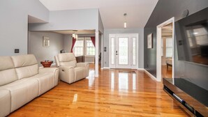 A spacious living room with a large flat-screen TV, a leather sofa, a recliner, and hardwood flooring. - Big Sky Retreat - Home for 10 (Fairfield)