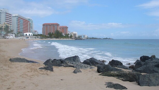 A beach with a rocky shoreline, a sandy beach, and buildings in the background. - Privilege Apartment @ San Juan Convention Center with A/C, parking and Wi-Fi (San Juan)