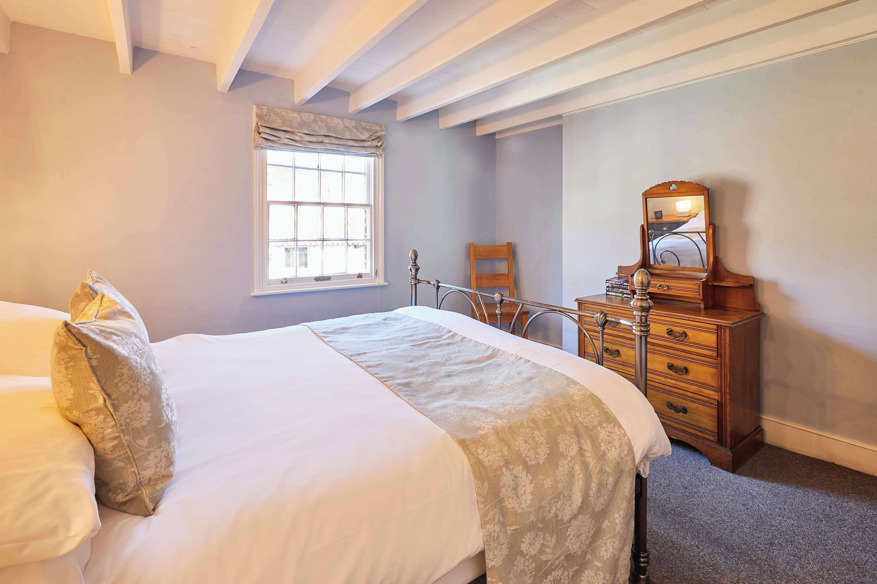 A bedroom with a bed, a dresser, a mirror, and a window.