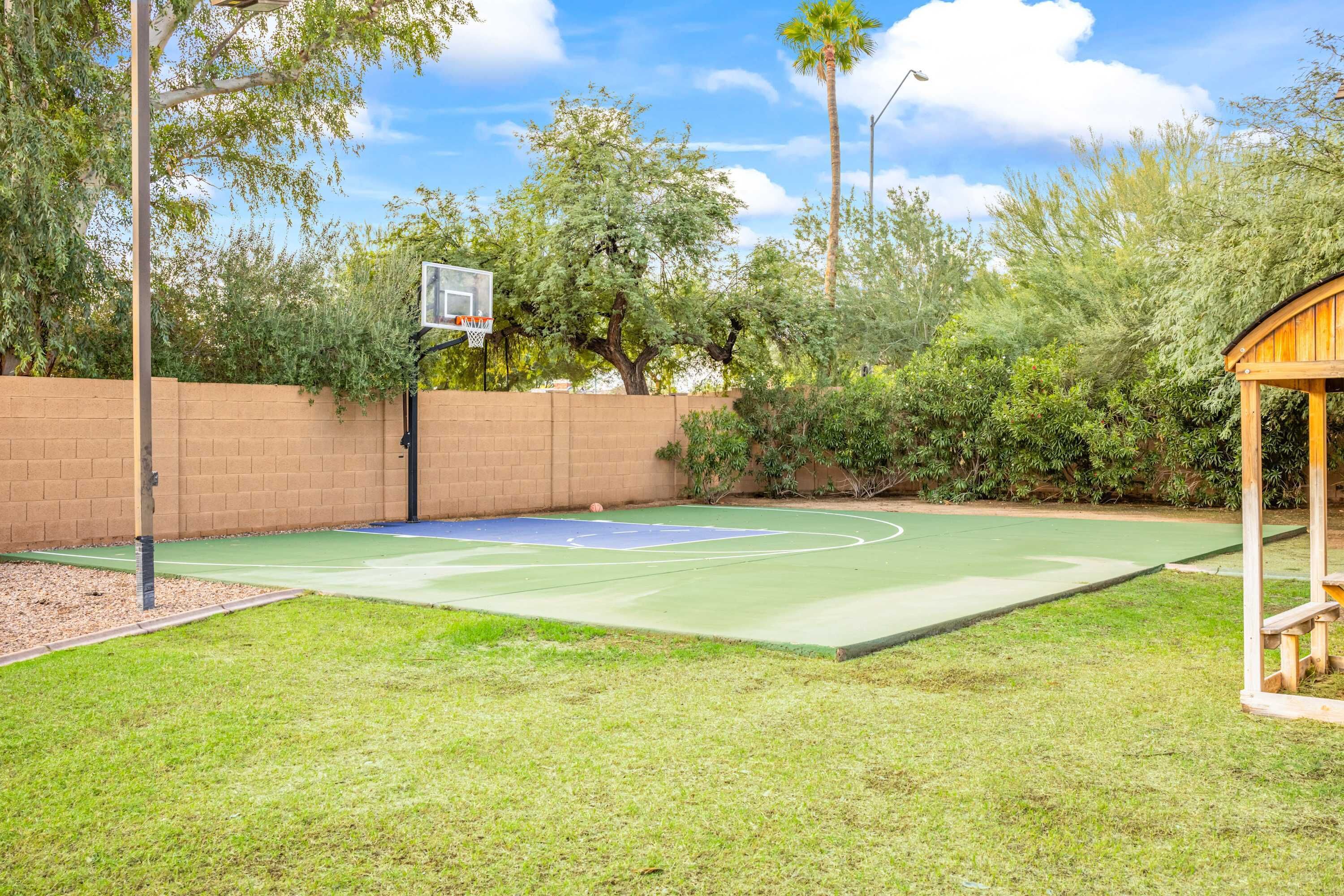 An outdoor basketball court with a wooden pavilion, surrounded by a brick wall and lush greenery.