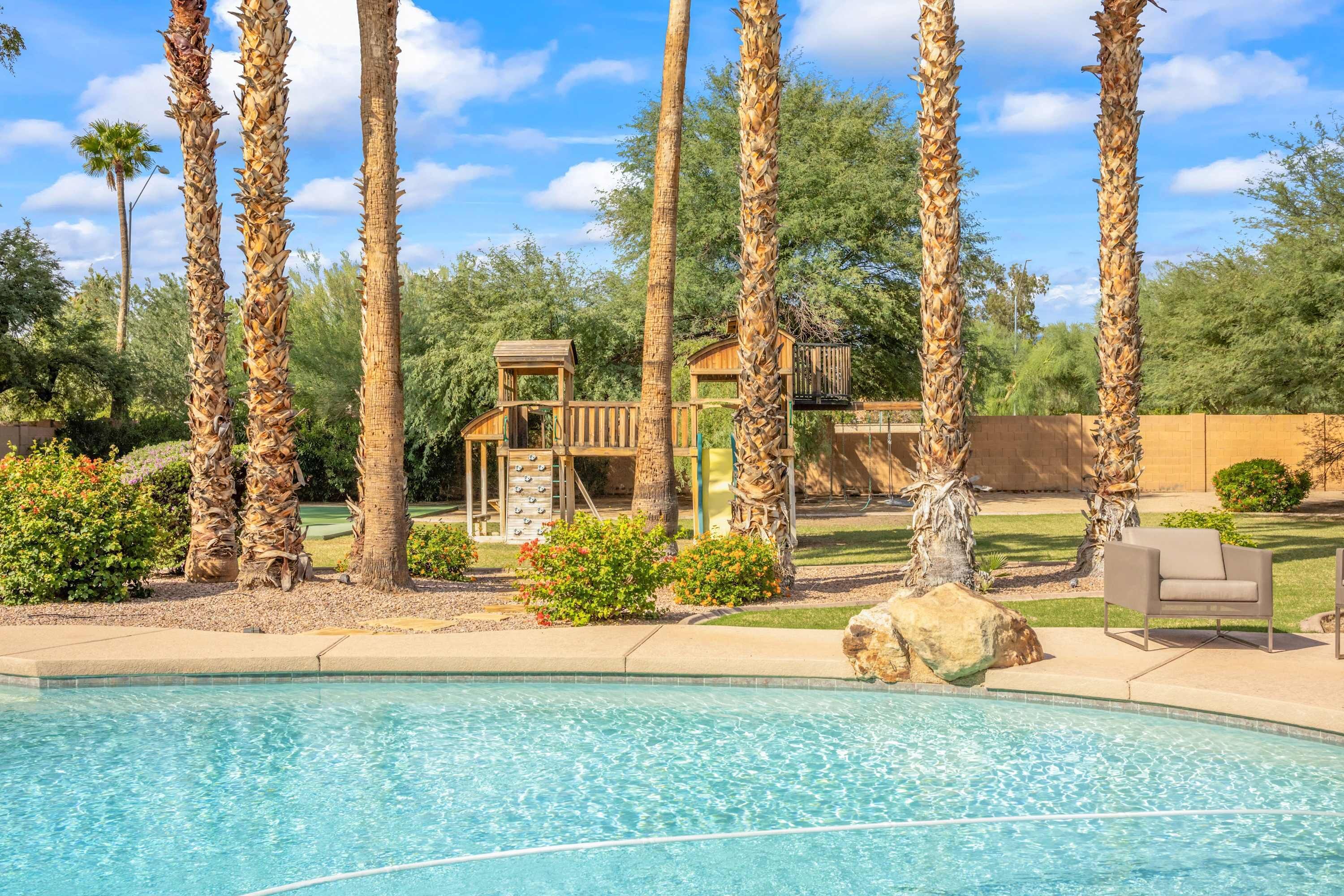 A swimming pool surrounded by tall palm trees and a wooden play structure.