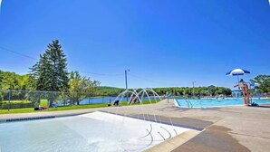 Zona de piscina con tobogán acuático, puesto de socorrista y vista a un lago.