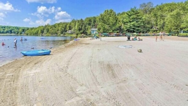 Una playa con arena, un bote pequeño y gente en el agua.
