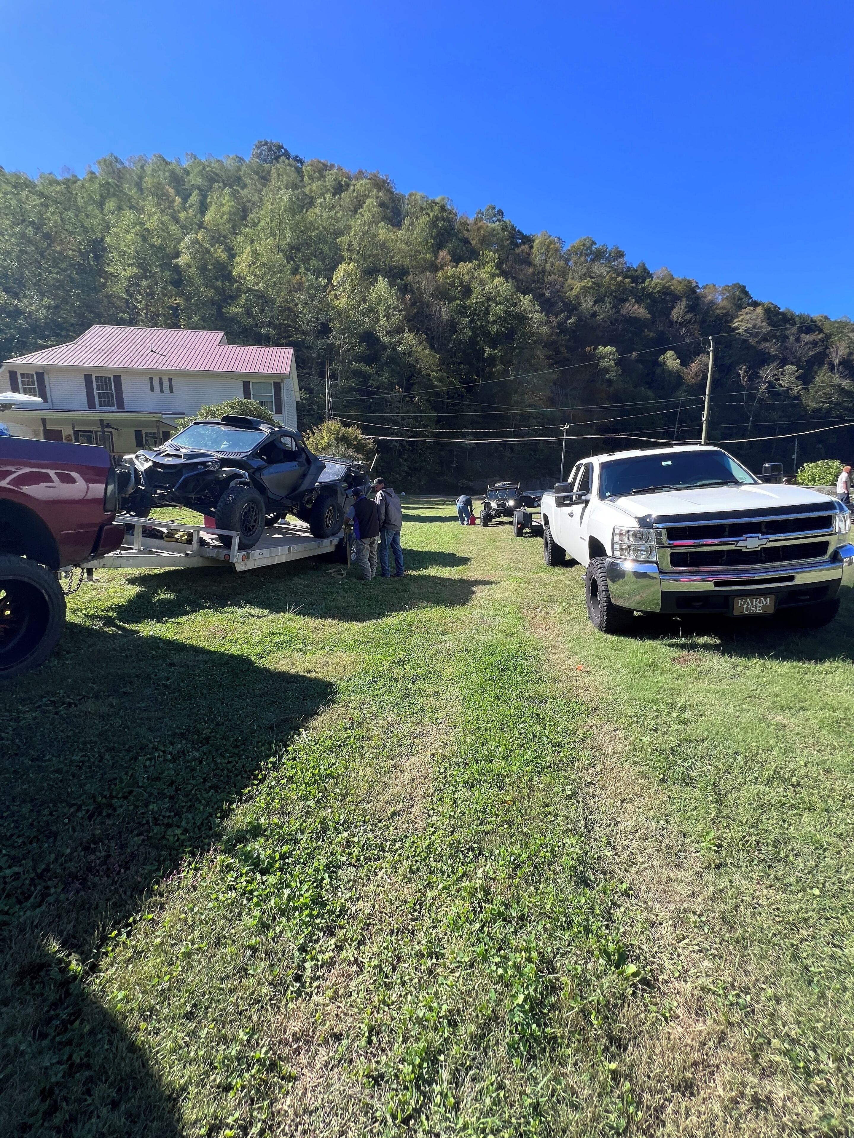A grassy area with a white pickup truck and a damaged vehicle on a trailer.
