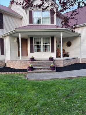 A two-story house with a porch, steps, and potted plants. - Large spacious house with ample parking for large groups. (Delbarton)