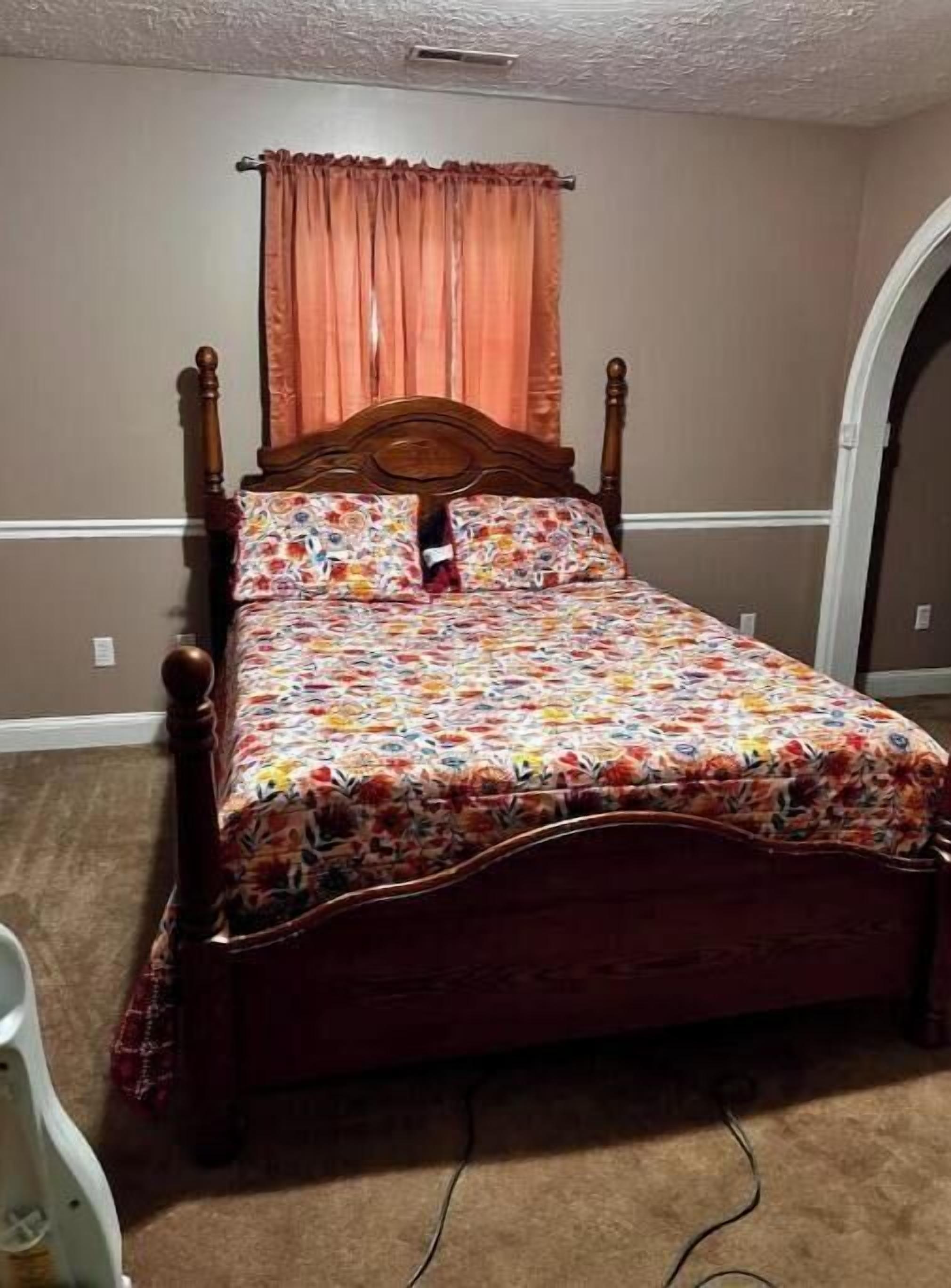 Une chambre à coucher avec un lit à baldaquin en bois, une couvre-lit à motifs floraux et un seul oreiller rouge.
