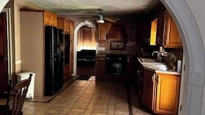 A kitchen with wooden cabinets, a black refrigerator, and a tiled floor. - Large spacious house with ample parking for large groups. (Delbarton)