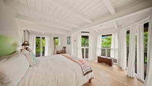 A spacious bedroom with a large bed, a bench, and a view of the outdoors through large windows. - Hale Kailea, Beautiful Hanalei Home TVNC#4241 (Hanalei)