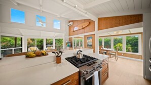 A modern kitchen with a large island, a gas stove, and a view of lush greenery. - Hale Kailea, Beautiful Hanalei Home TVNC#4241 (Hanalei)