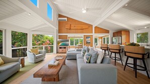 A spacious living area with a high ceiling, a large window, and a kitchen area with bar stools. - Hale Kailea, Beautiful Hanalei Home TVNC#4241 (Hanalei)