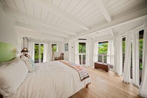 A spacious bedroom with a large bed, a bench, and a view of the outdoors through large windows.