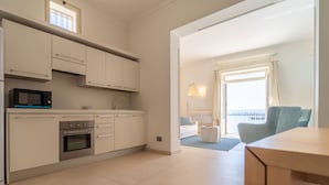 Een moderne keuken met witte kasten, een magnetron en een oven. Er is een eethoek met een tafel en stoelen, en een balkon met uitzicht.