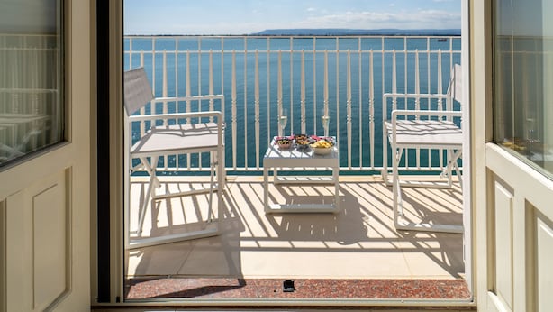 Een balkon met twee witte stoelen, een kleine tafel met eten en drinken, en uitzicht op de zee.