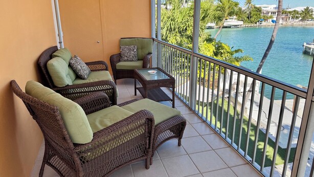 A balcony with wicker furniture, a view of a body of water, and a clear sky.