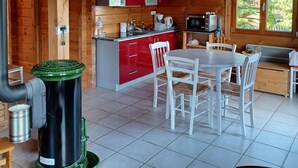 Interior de una cabaña de madera con cocina, comedor y un ventanal grande.