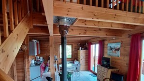 Interior de una cabaña de madera con escalera, chimenea, comedor y sala de estar con sofá y mesa.