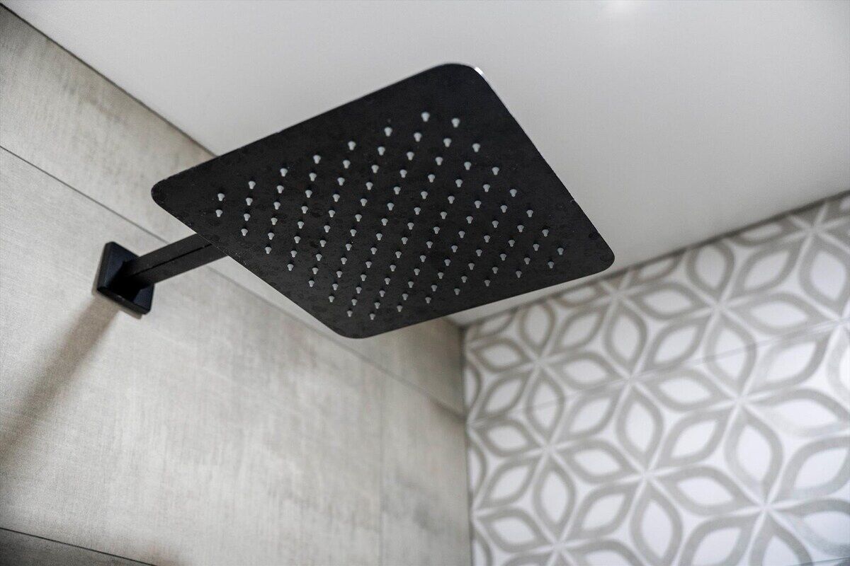 A black showerhead mounted on a wall with a geometric patterned tile design in the background.