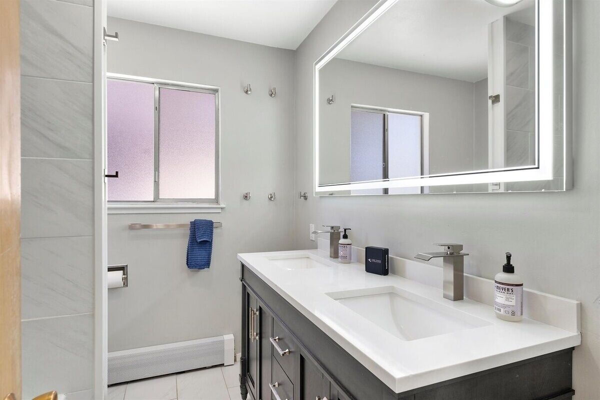 Een moderne badkamer met een grote spiegel, twee wastafels en een handdoekrek.