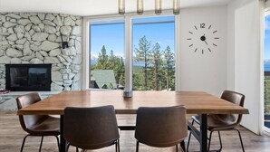 A dining area with a stone wall, a fireplace, and a large window with a view of trees and mountains. - Hch1083 - Mountain Serenity 4 Bedroom Home (South Lake Tahoe)