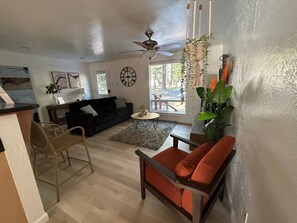 A living room with a black sofa, a wooden chair, a coffee table, and a hanging plant. - Coh0957 - Bella Ari 3 Bedroom Home (South Lake Tahoe)