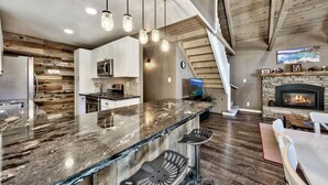 A modern kitchen with a marble countertop, wooden accents, and a stone fireplace. - Cyh0876 - Island Cabin 3 Bedroom Cabin (South Lake Tahoe)