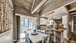 A modern kitchen with wooden beams, a dining area with a table and chairs, and a view of the outdoors. - Cyh0876 - Island Cabin 3 Bedroom Cabin (South Lake Tahoe)
