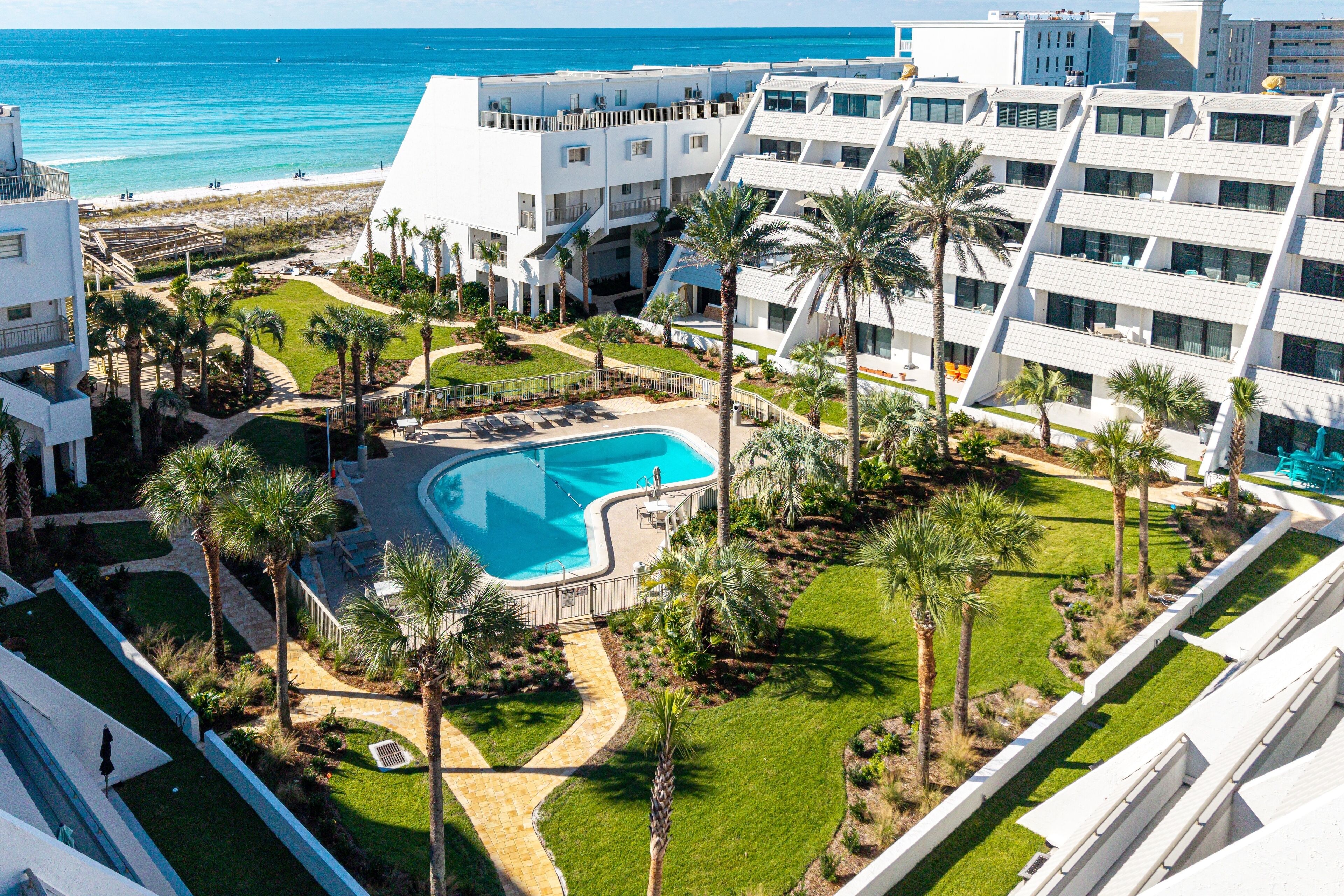Un resort con piscina rodeada de palmeras y vista al mar.
