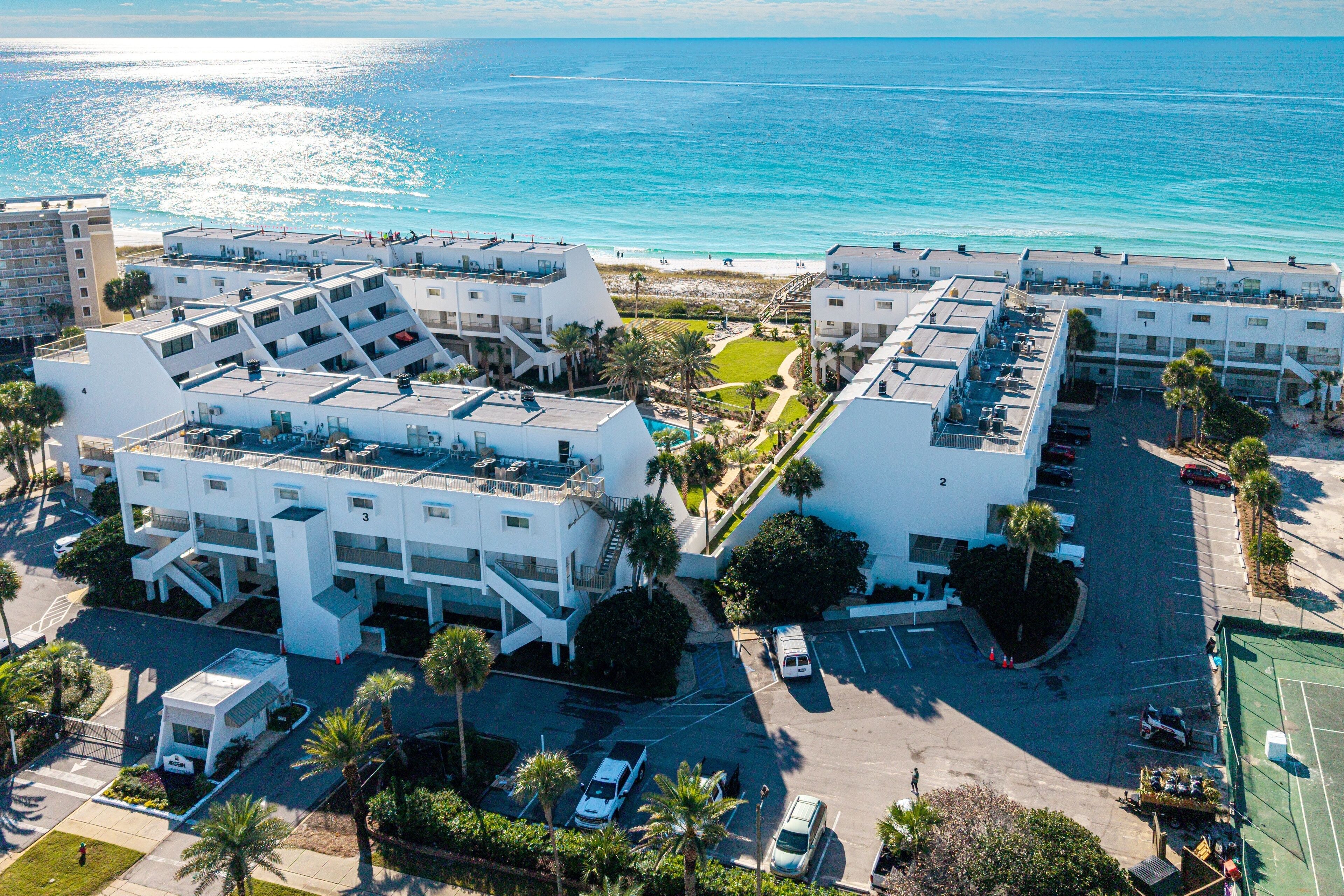 Ein Luftbild eines Hotelkomplexes an der Küste mit mehreren Gebäuden, einem Parkplatz und einem Strand im Hintergrund.