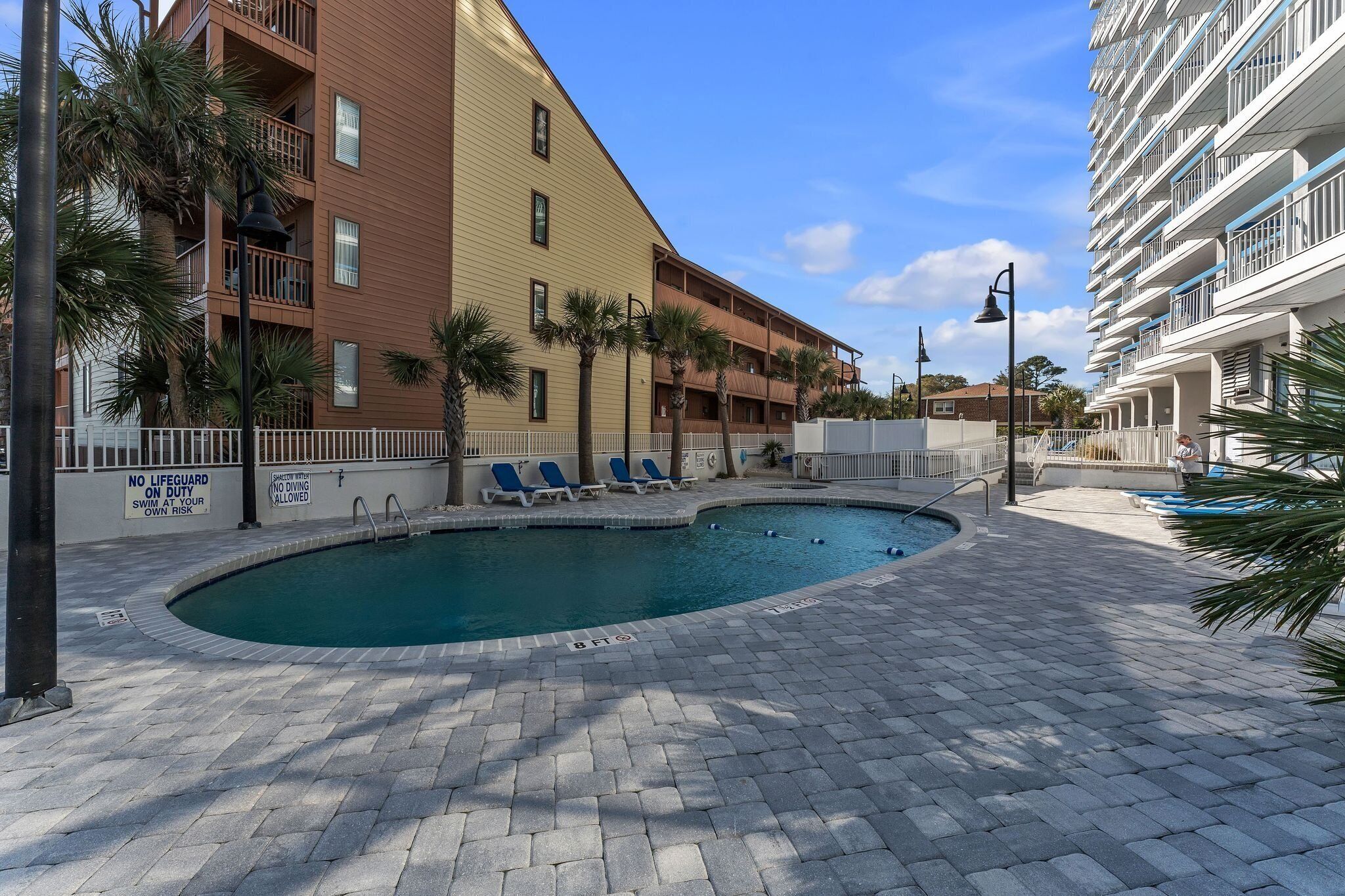 A pool area with lounge chairs, palm trees, and a building with balconies.