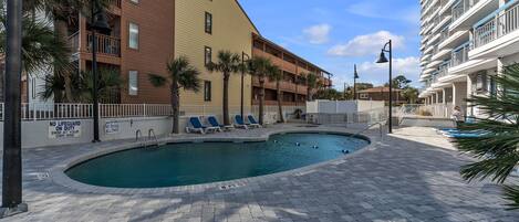 A pool area with lounge chairs, palm trees, and a building with balconies.