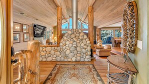 Ein rustikaler Innenraum mit Kamin aus Stein, Holzbalken und einer gemütlichen Sitzecke.