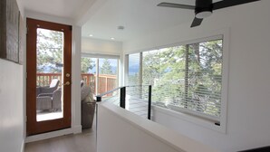 A modern interior with a wooden door leading to an outdoor area, a ceiling fan, and large windows with blinds.