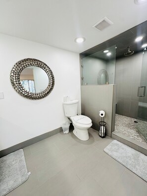 A bathroom with a toilet, a round mirror, a shower with glass doors, and a small trash bin. - Lvc0615 - Lake Therapy 3 Bedroom Condo (Zephyr Cove)