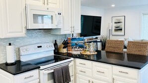 A kitchen with white cabinetry, a black countertop, a stove, an oven, and a microwave.