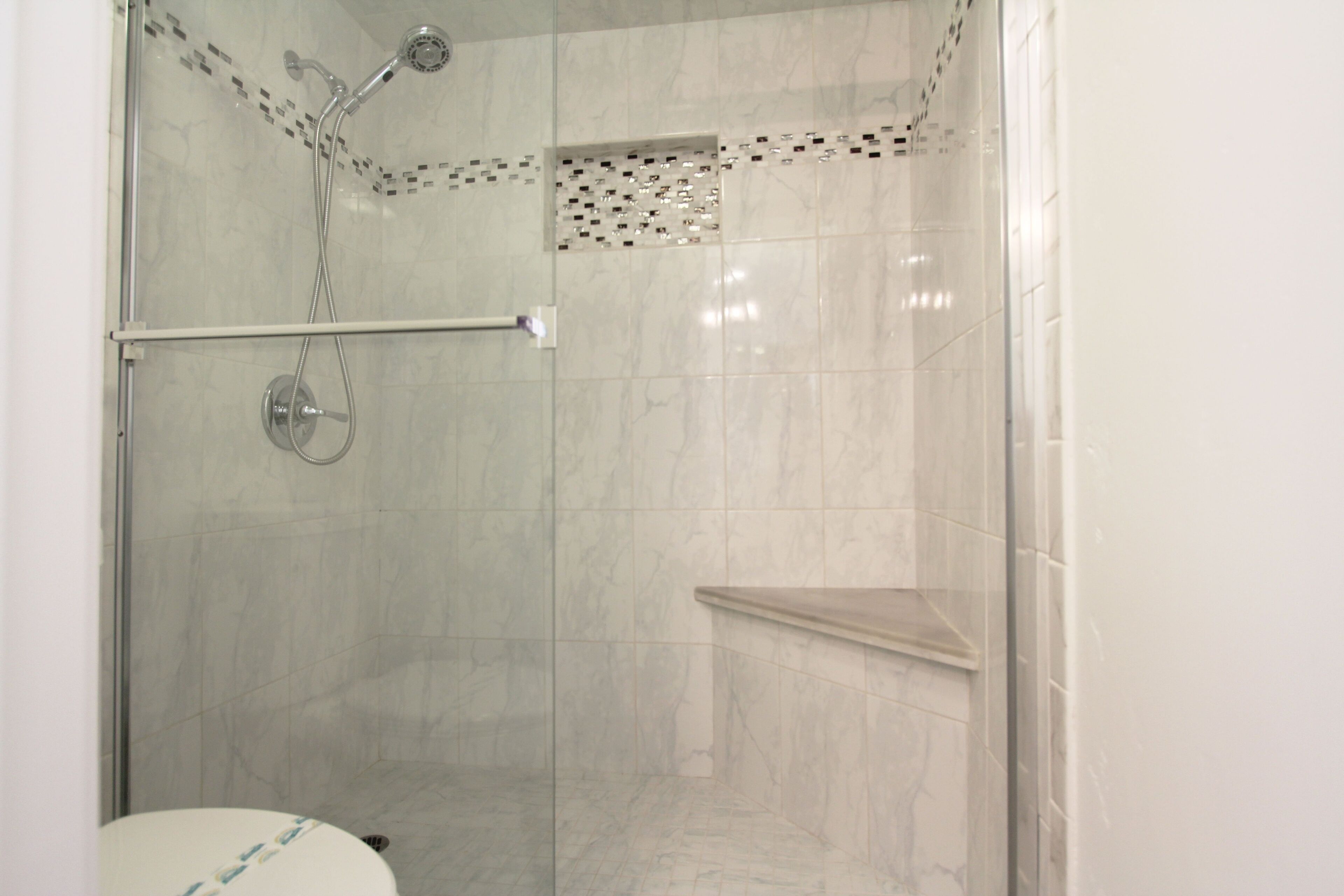 Ducha con puerta de vidrio, cabezal de ducha de mano y grifo empotrado.