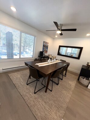 A modern dining area with a dark wood table, four chairs, a ceiling fan, and a large window with blinds. - Lvc0615 - Lake Therapy 3 Bedroom Condo (Zephyr Cove)