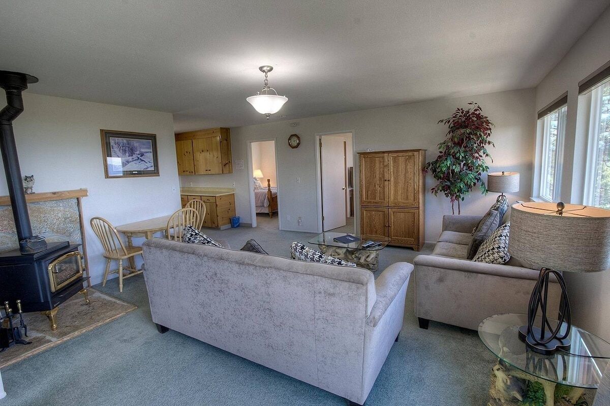 A cozy living room with a fireplace, a sofa, a glass coffee table, and a dining area with wooden cabinets and chairs.