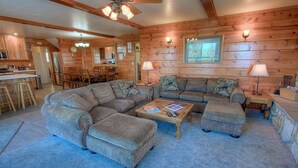 A cozy log cabin interior with a sectional sofa, ottomans, a coffee table, a dining area, and a kitchen. - Hch1475 - Heavenly Lake View Retreat 5 Bedroom Home (South Lake Tahoe)