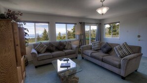A living room with two sofas, a glass coffee table, and large windows offering a view of trees and mountains. - Hch1475 - Heavenly Lake View Retreat 5 Bedroom Home (South Lake Tahoe)
