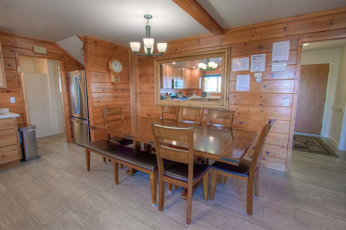 A wooden-paneled dining room with a large table and chairs, a refrigerator, and a clock on the wall.