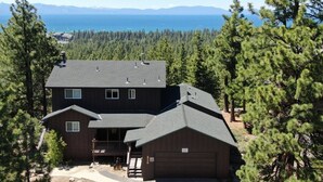 A two-story house with a dark roof, surrounded by dense forest and a view of the ocean. - Hch1475 - Heavenly Lake View Retreat 5 Bedroom Home (South Lake Tahoe)
