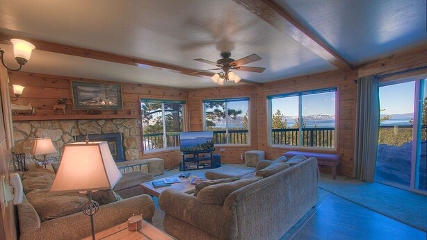 A cozy living room with a stone fireplace, comfortable seating, and large windows offering a scenic view. - Hch1475 - Heavenly Lake View Retreat 5 Bedroom Home (South Lake Tahoe)